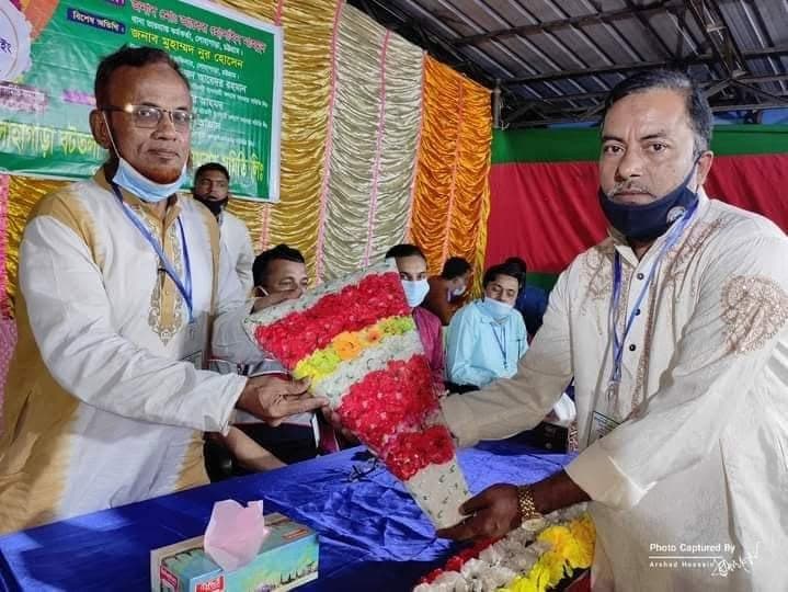 মঞ্চে একজন অতিথির হাতে ফুলের তোড়া তুলে দেওয়া হচ্ছে
