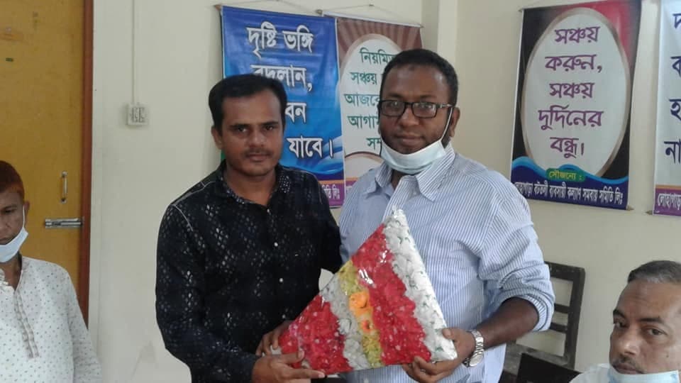 অফিসে ফুলের তোড়া দিয়ে শুভেচ্ছা; পেছনের পোস্টারে লেখা "সঞ্চয় করুন, সঞ্চয় দুর্দিনের বন্ধু"