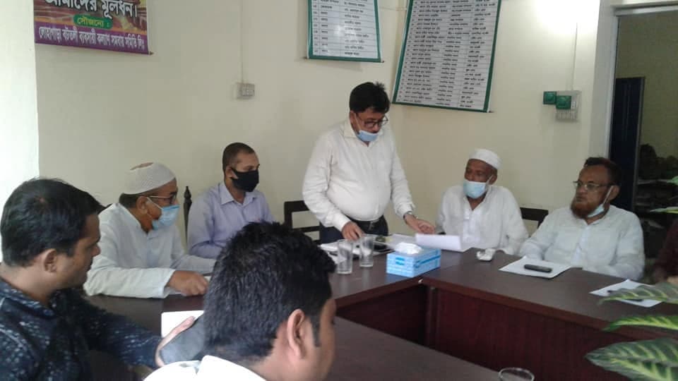 অফিসের সভায় একজন দাঁড়িয়ে কথা বলছেন, অন্যরা টেবিলে বসে শুনছেন